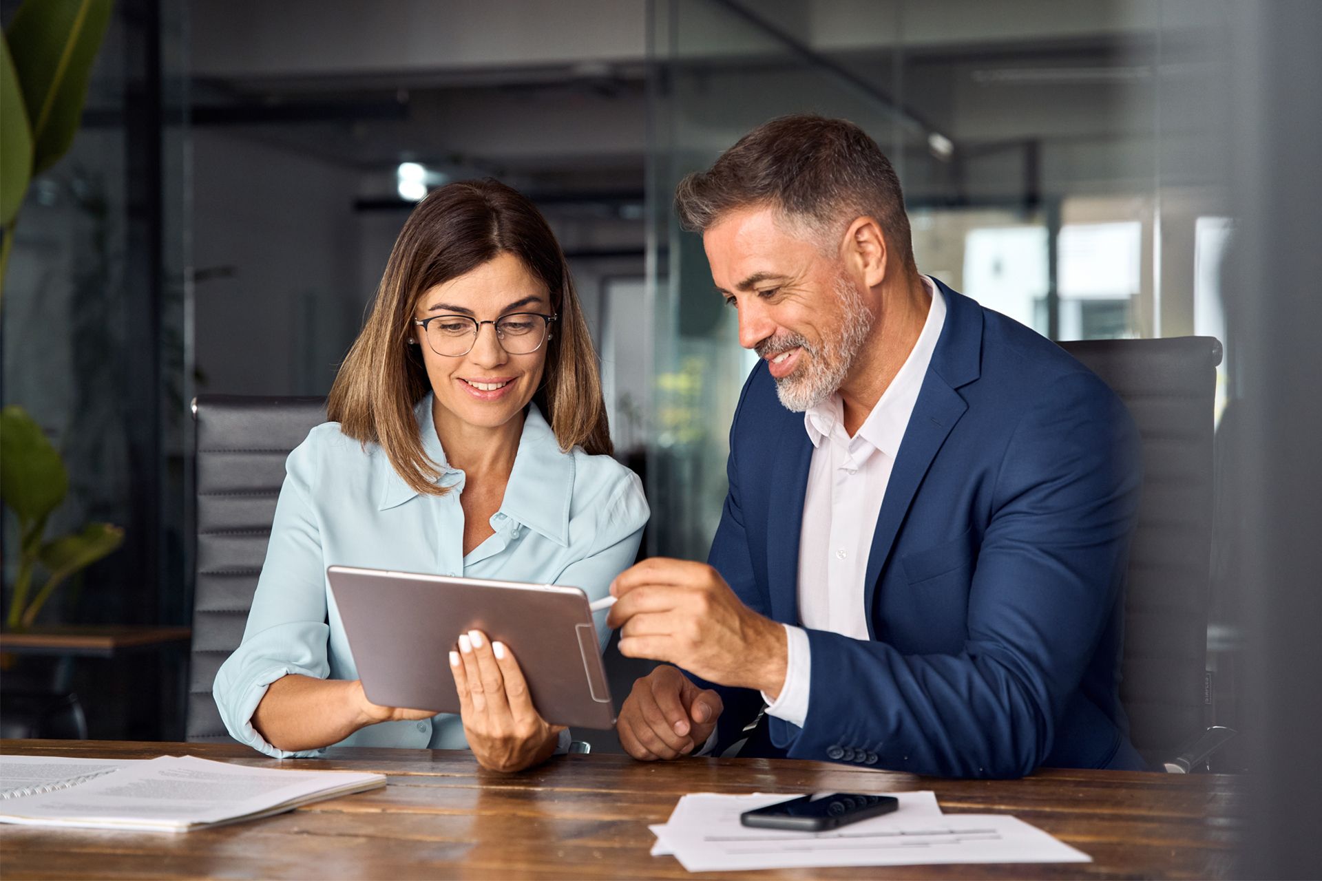 People in business attire at a conference table with laptops, talking in a modern office.