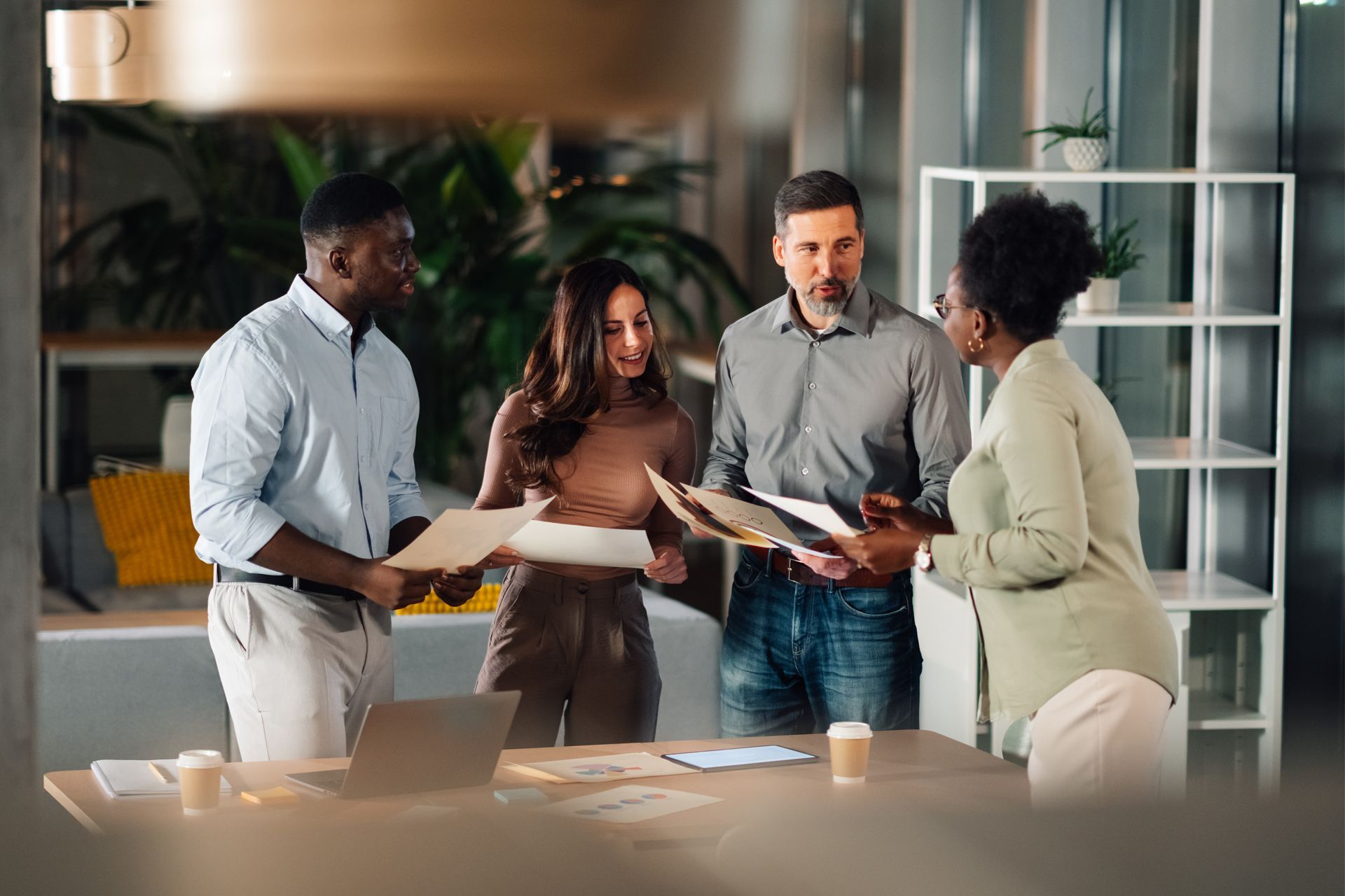 Four people in an office, discussing documents at a table.