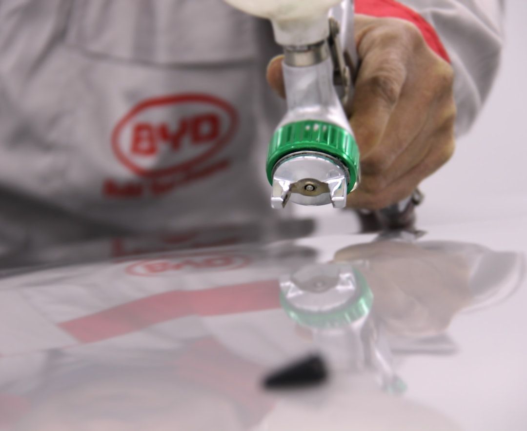 Person holding a spray gun, focused on applying paint to a reflective surface, likely automotive, indoors.