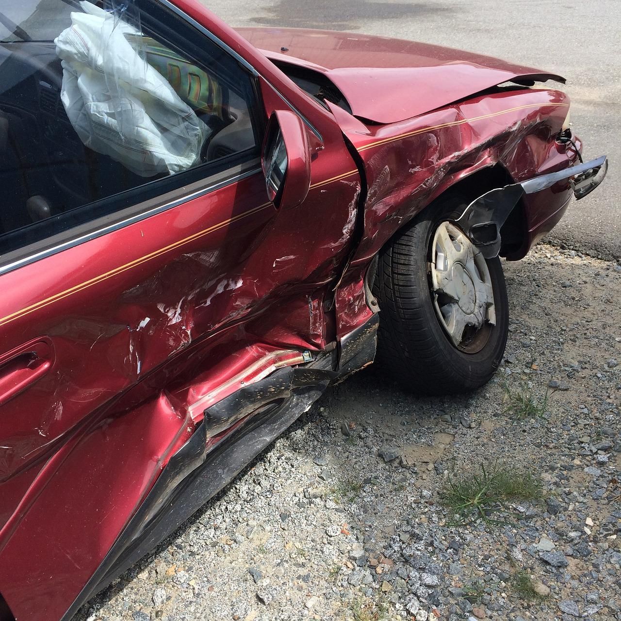 Red car with significant damage to the front driver's side after a collision. Airbag deployed.