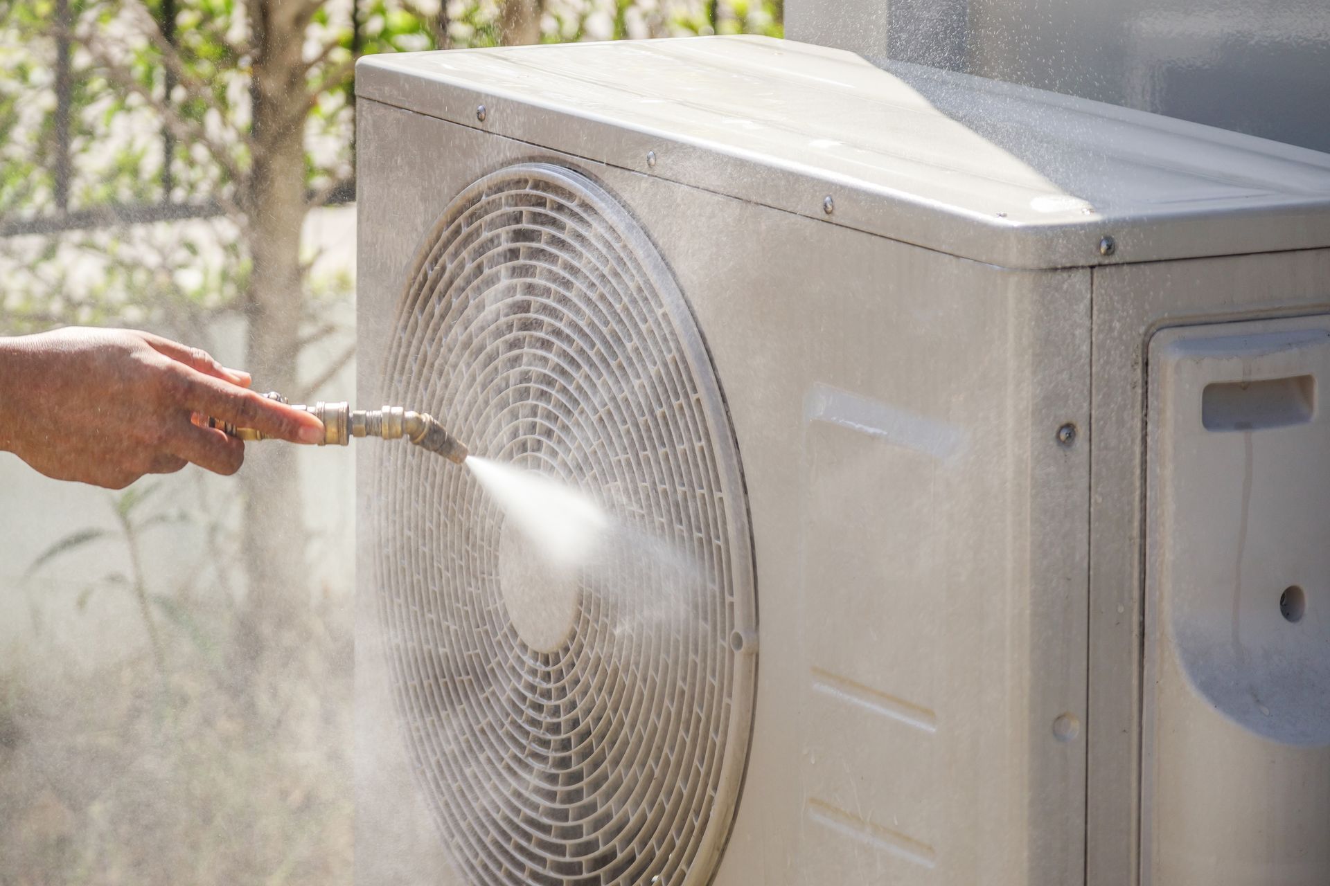 A person is cleaning an air conditioner with a hose.