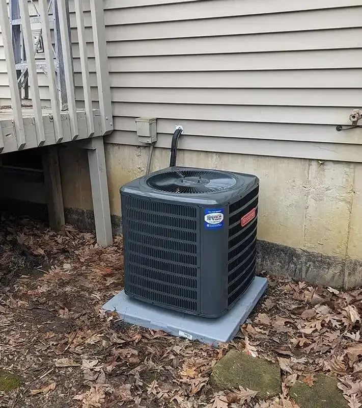 An air conditioner is sitting on top of a concrete platform in front of a house.