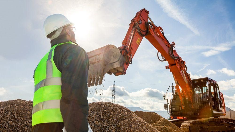 A Construction Worker Is Standing in Front of An Excavator at A Construction Site — Hillery Group in Bowen, QLD