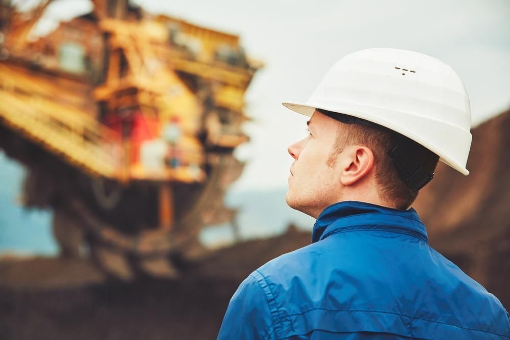 A Man Wearing a Hard Hat Is Standing in Front of A Large Excavator — Hillery Group in Bowen, QLD