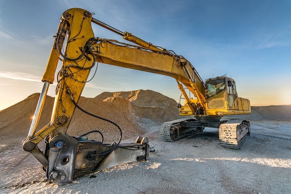 A Yellow Excavator Is Sitting in Front of A Pile of Gravel — Hillery Group in Bowen, QLD