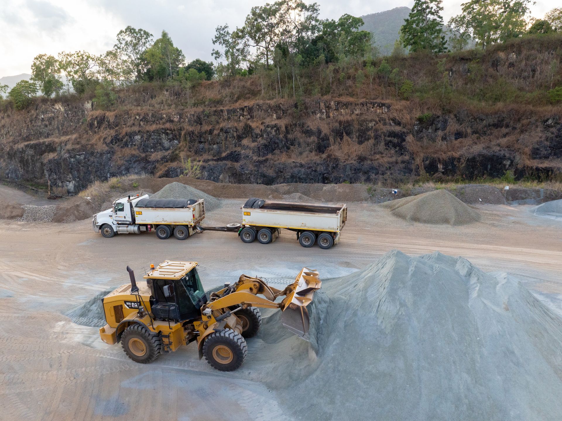 A Large Yellow Excavator Is Working on A Dirt Field — Hillery Group in Bowen, QLD