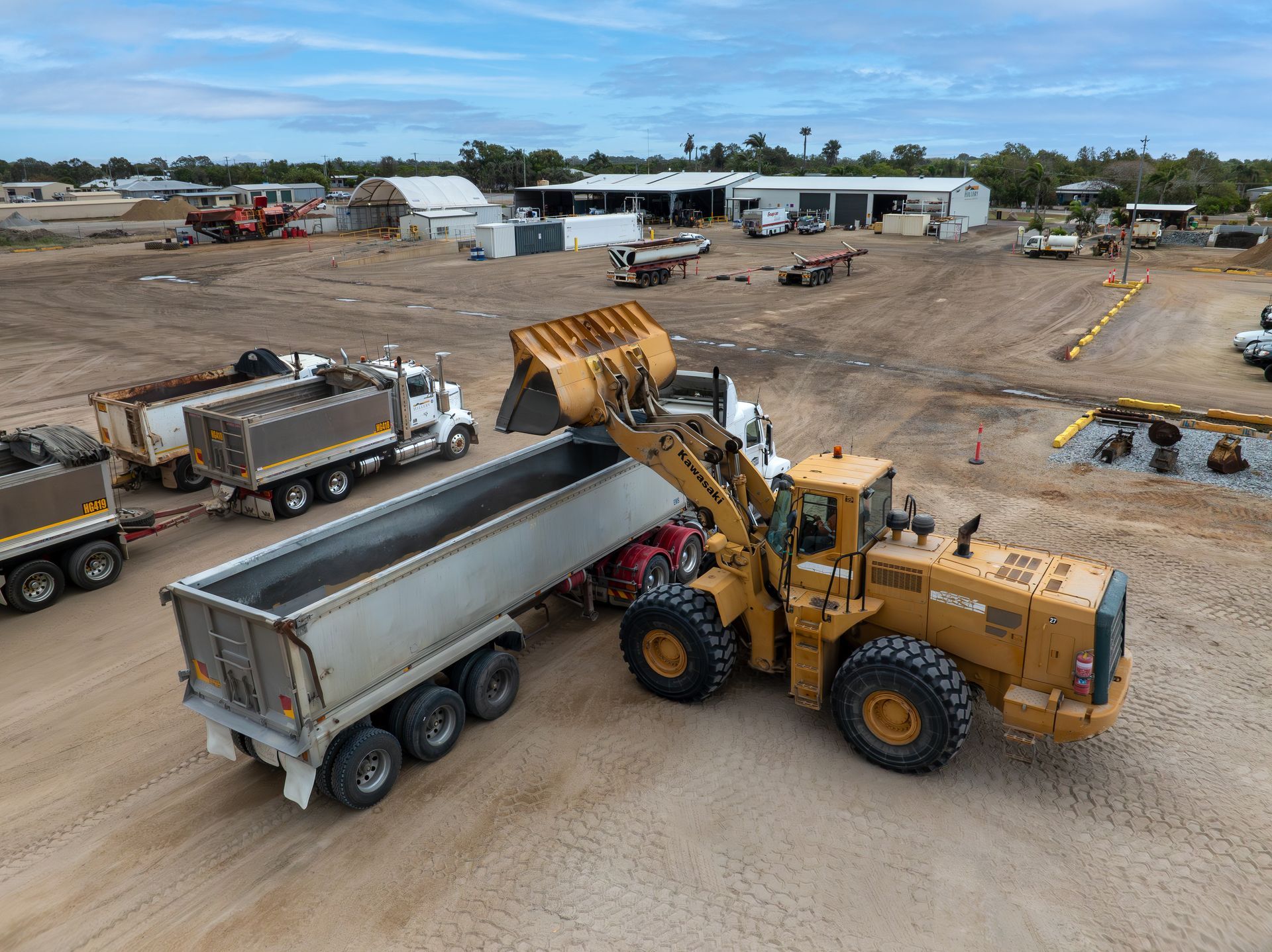 A Man Wearing a Hard Hat Is Standing in Front of A Large Excavator — Hillery Group in Bowen, QLD