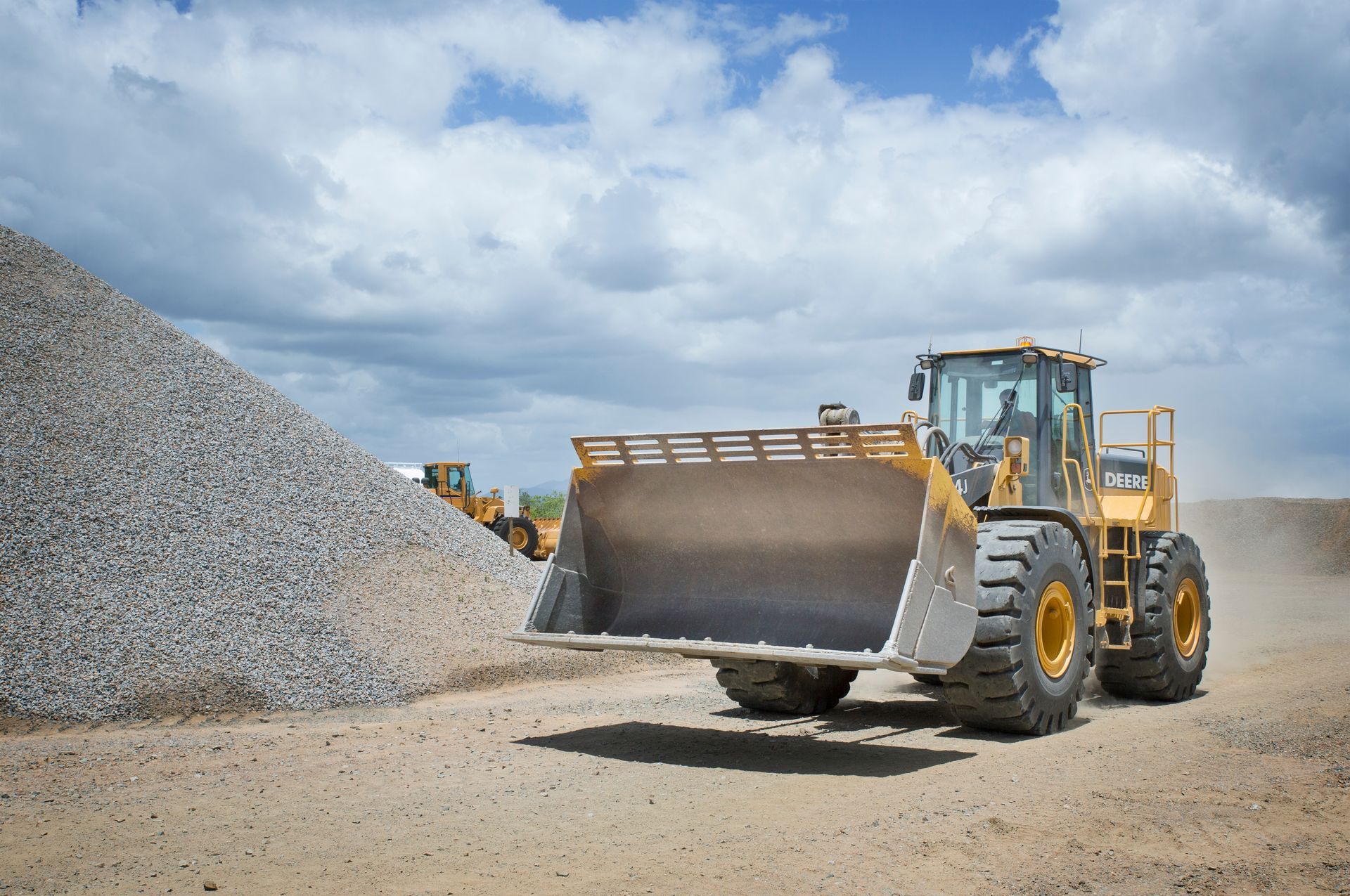 A Yellow Digger is Driving Through a Dirt Field — Hillery Group in Gordons, QLD