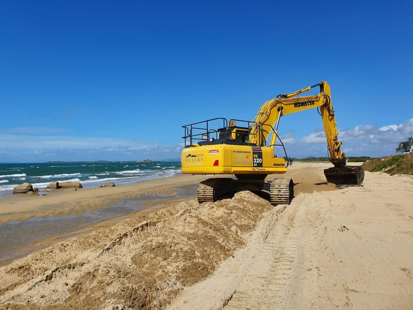 A Yellow Excavator Is Working on A Sandy Beach Near the Ocean — Hillery Group in Bowen, QLD