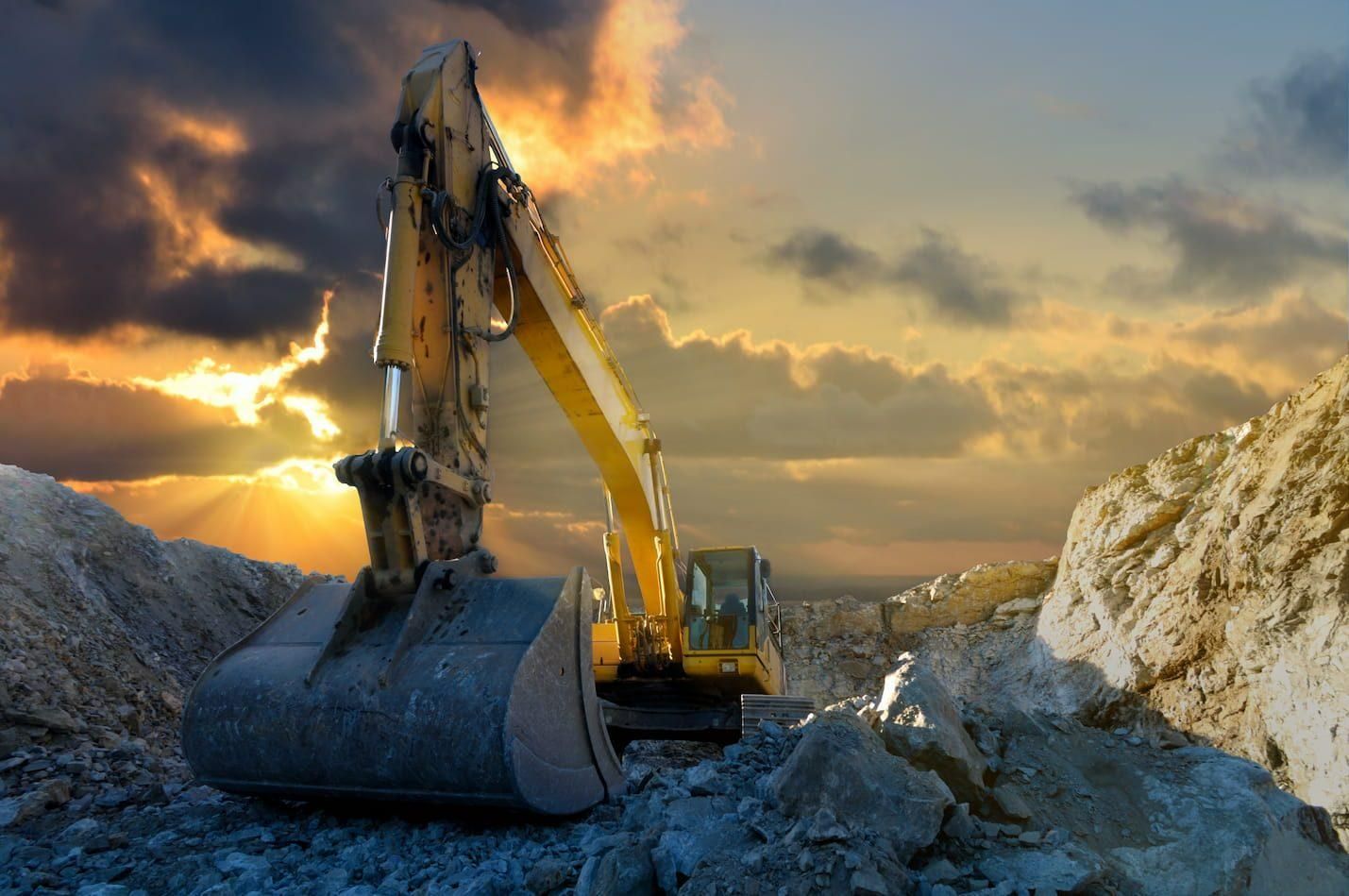A Yellow Excavator Is Working in A Rocky Area at Sunset — Hillery Group in Bowen, QLD