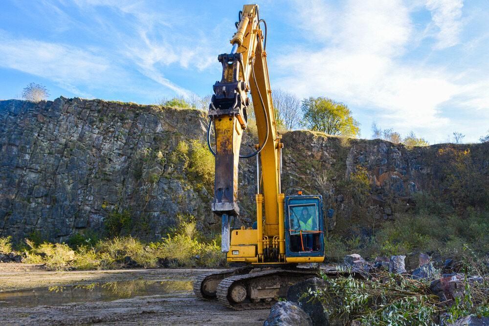 A Yellow Excavator is Sitting in a Dirt Field in Front of a Rock Wall — Hillery Group in Bowen, QLD