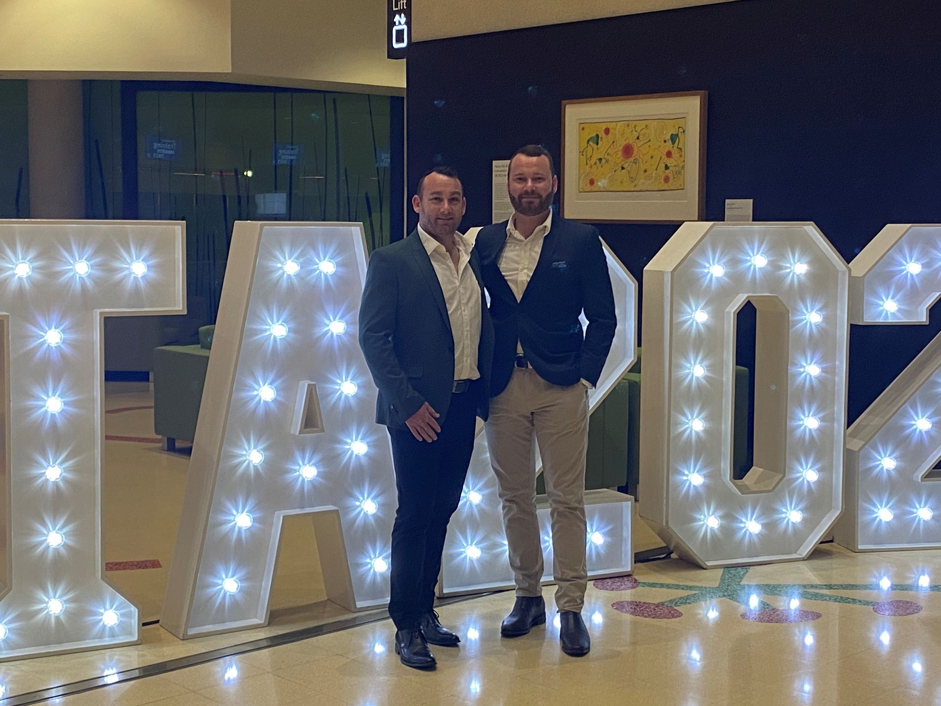 Two Men Are Standing In Front Of Large Lit Up Letters — Hillery Group In Bowen, Qld