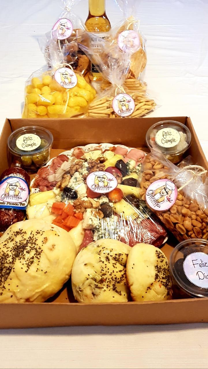 Caja de embutidos con varios aperitivos: queso, aceitunas, frutos secos, pan, galletas saladas y una botella de vino.