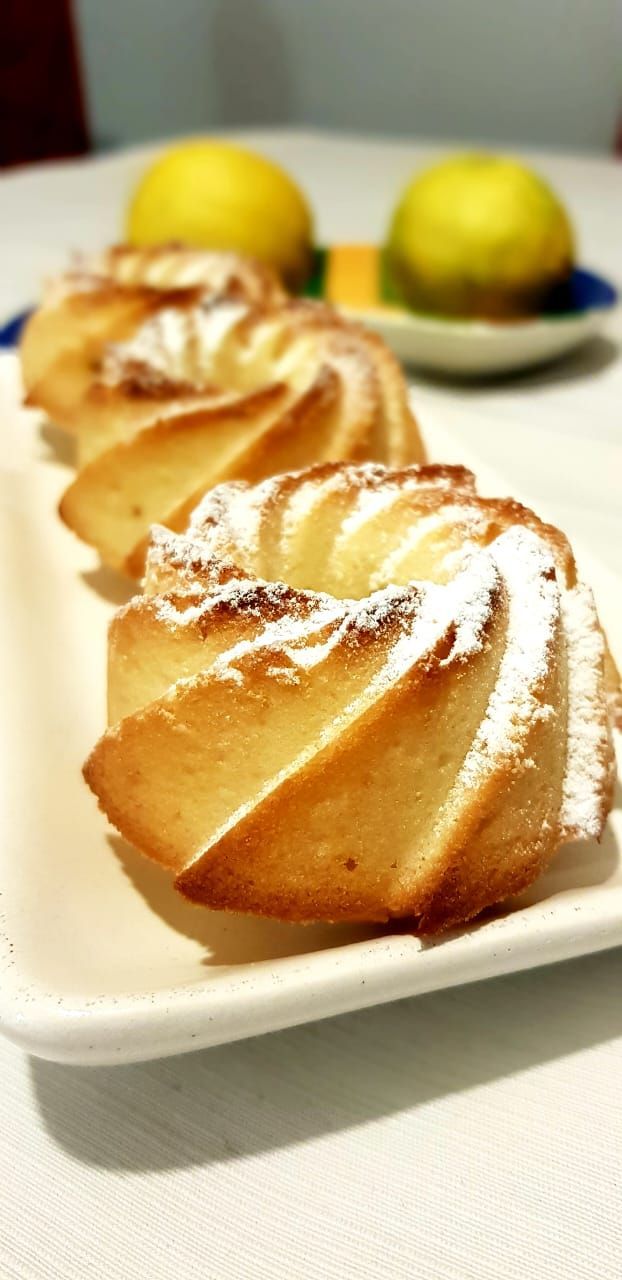 Tres pequeños bizcochos bundt espolvoreados con azúcar glas sobre un plato rectangular blanco con limones al fondo.