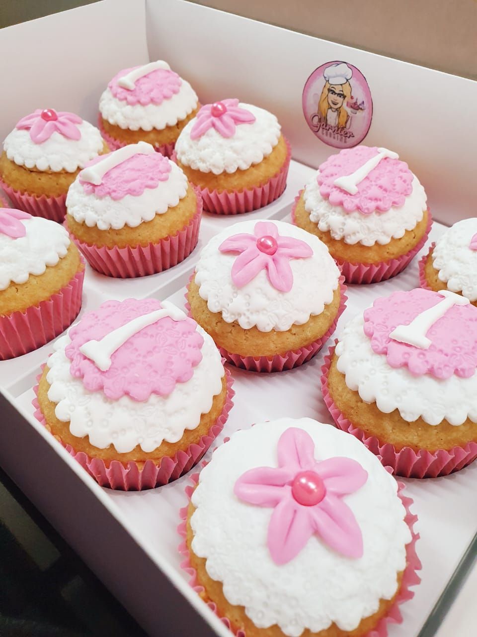 Magdalenas en envoltorios rosas, cubiertas con glaseado blanco, flores rosas y el número