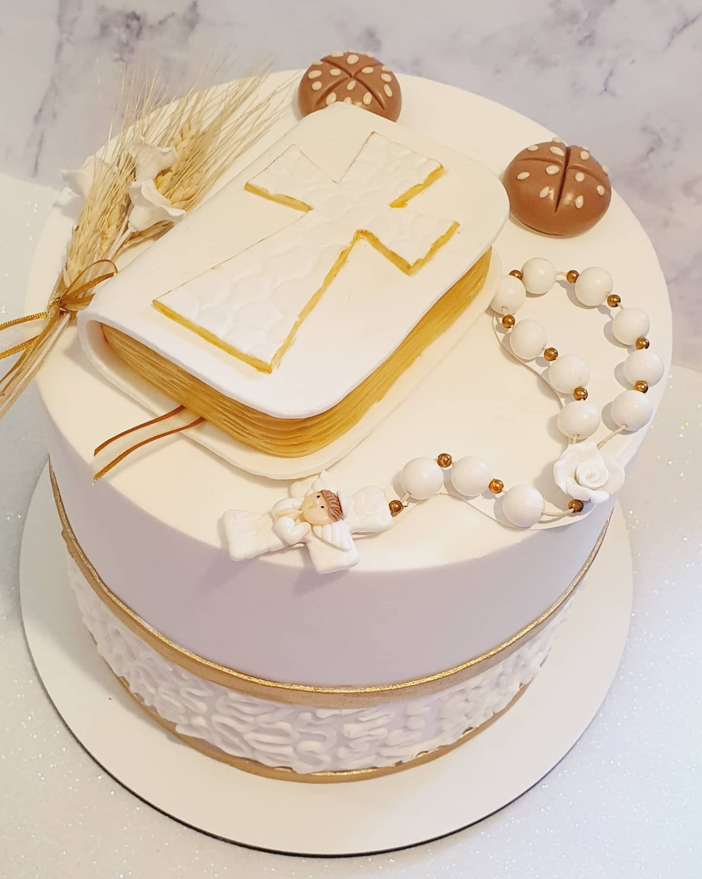 Pastel blanco decorado con un libro con una cruz, un rosario y hostias de comunión.