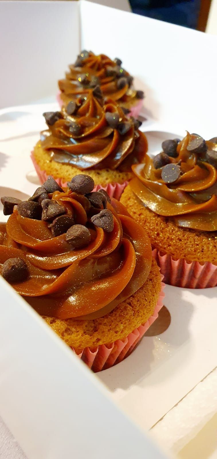 Magdalenas con glaseado marrón y pepitas de chocolate en una caja blanca.