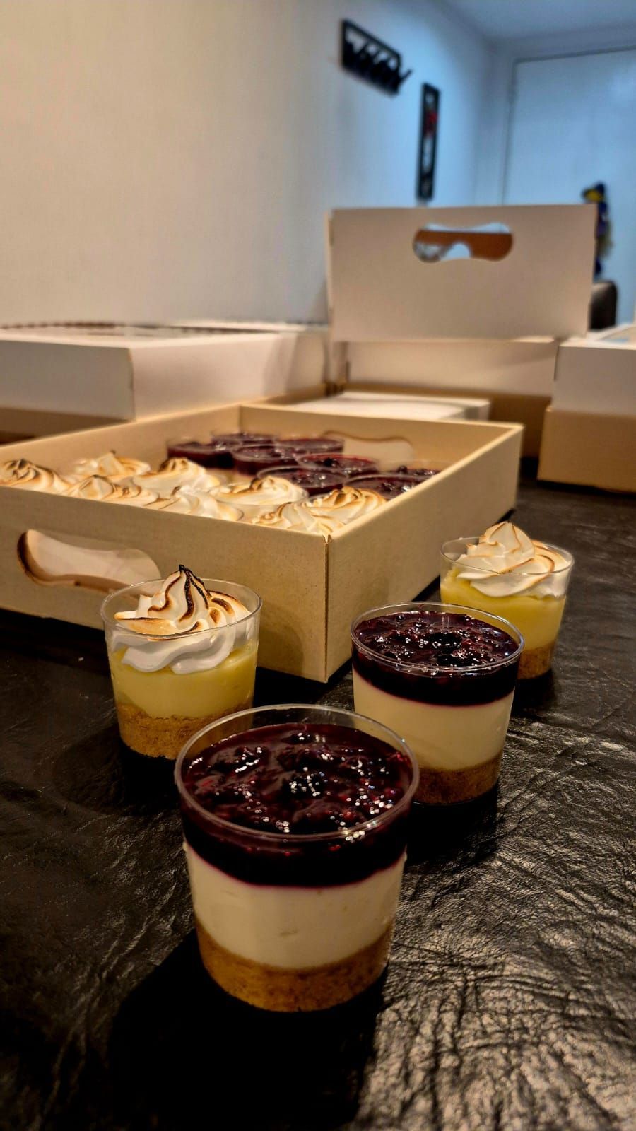 Postres en vasos transparentes y una bandeja de madera. Tarta de queso y merengue de limón sobre una superficie negra.