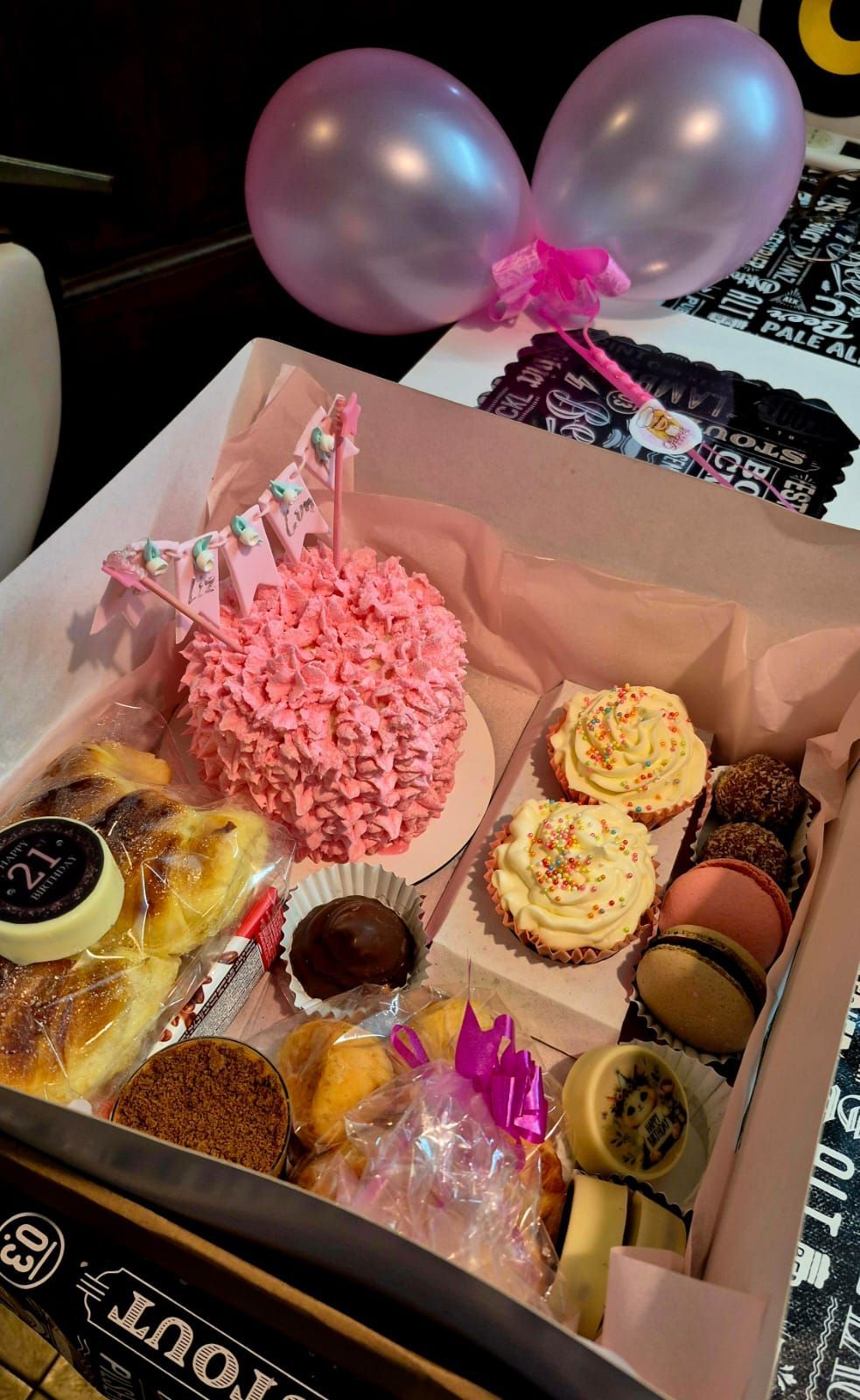 Caja de pasteles y tarta, tarta con glaseado rosa en forma de lencería, magdalenas, macarons, globos.