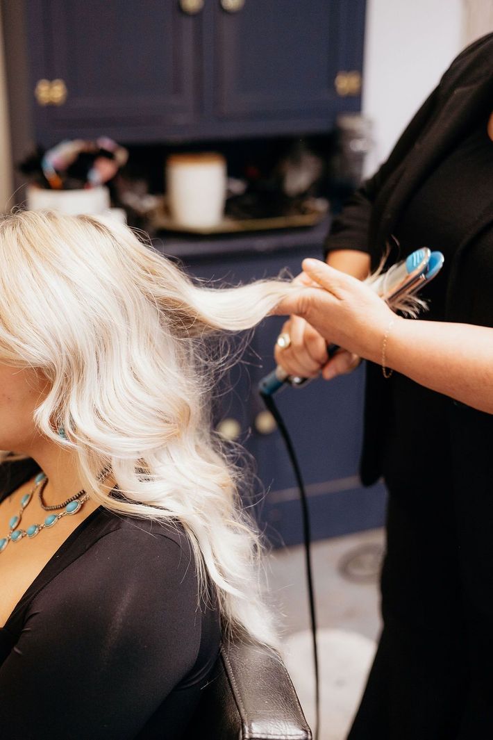 Stylist curling blonde hair with a curling iron in a salon.