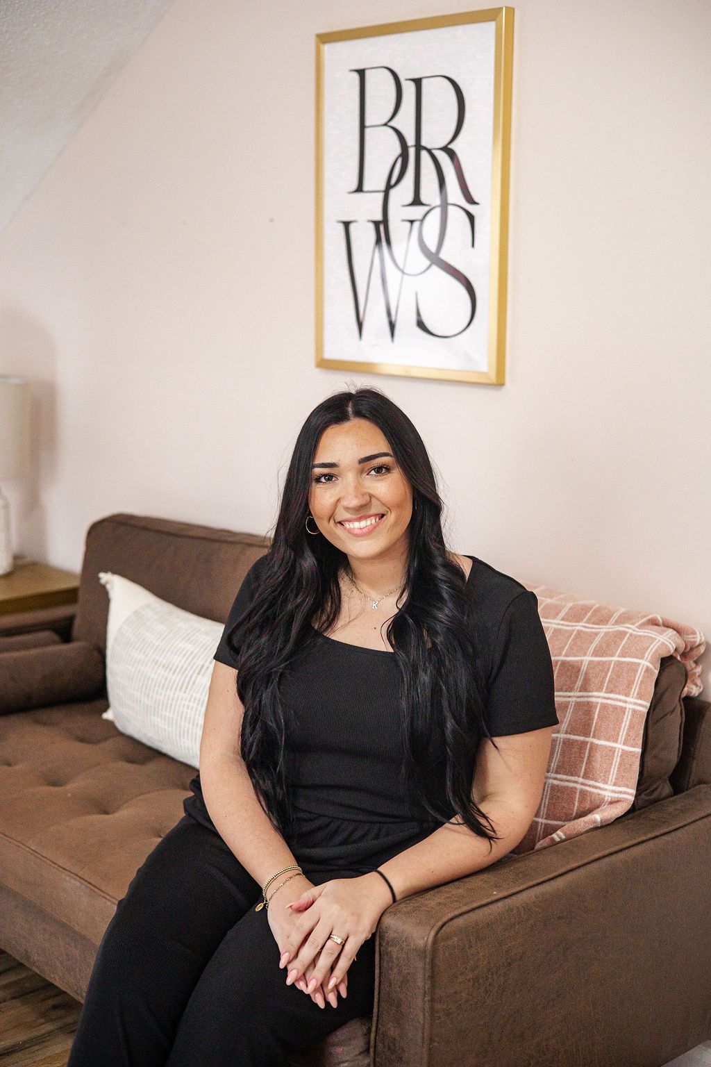 Woman smiling, sitting on a brown couch in a room with a 