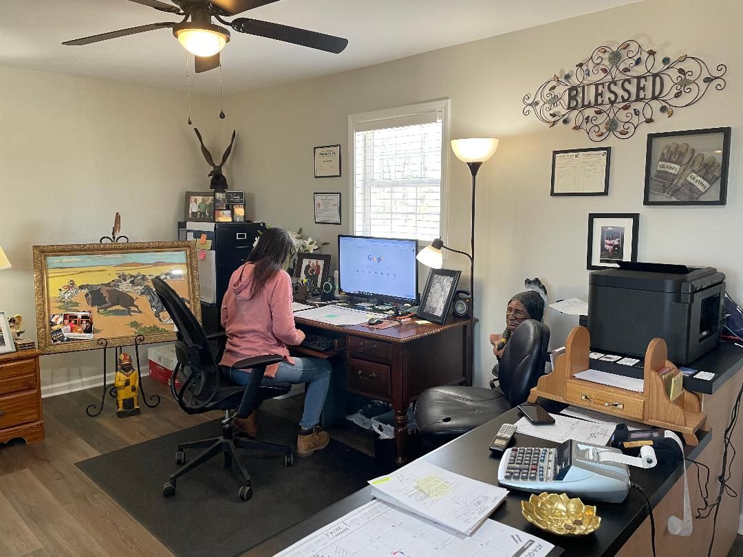 Woman working at a desk in a home office with another person. 