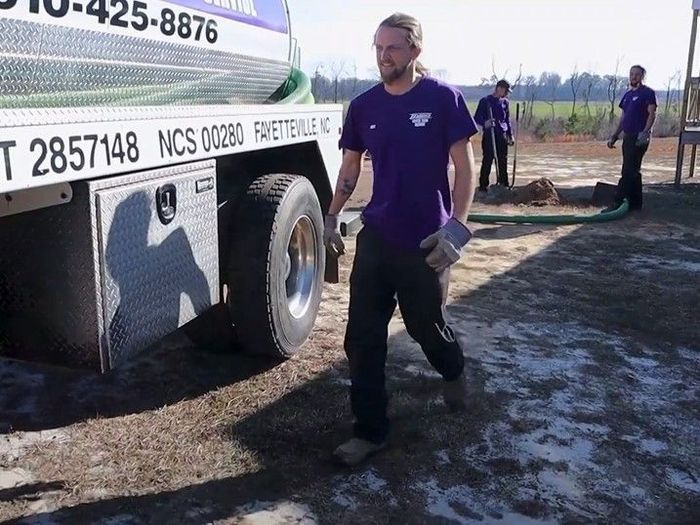 A man in a purple shirt is standing in front of a ncs truck