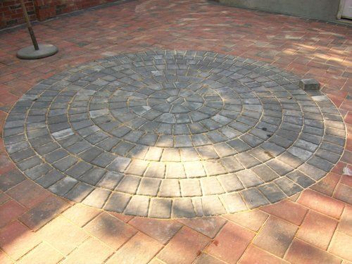 A circular pattern of bricks on a patio with a tree in the background.