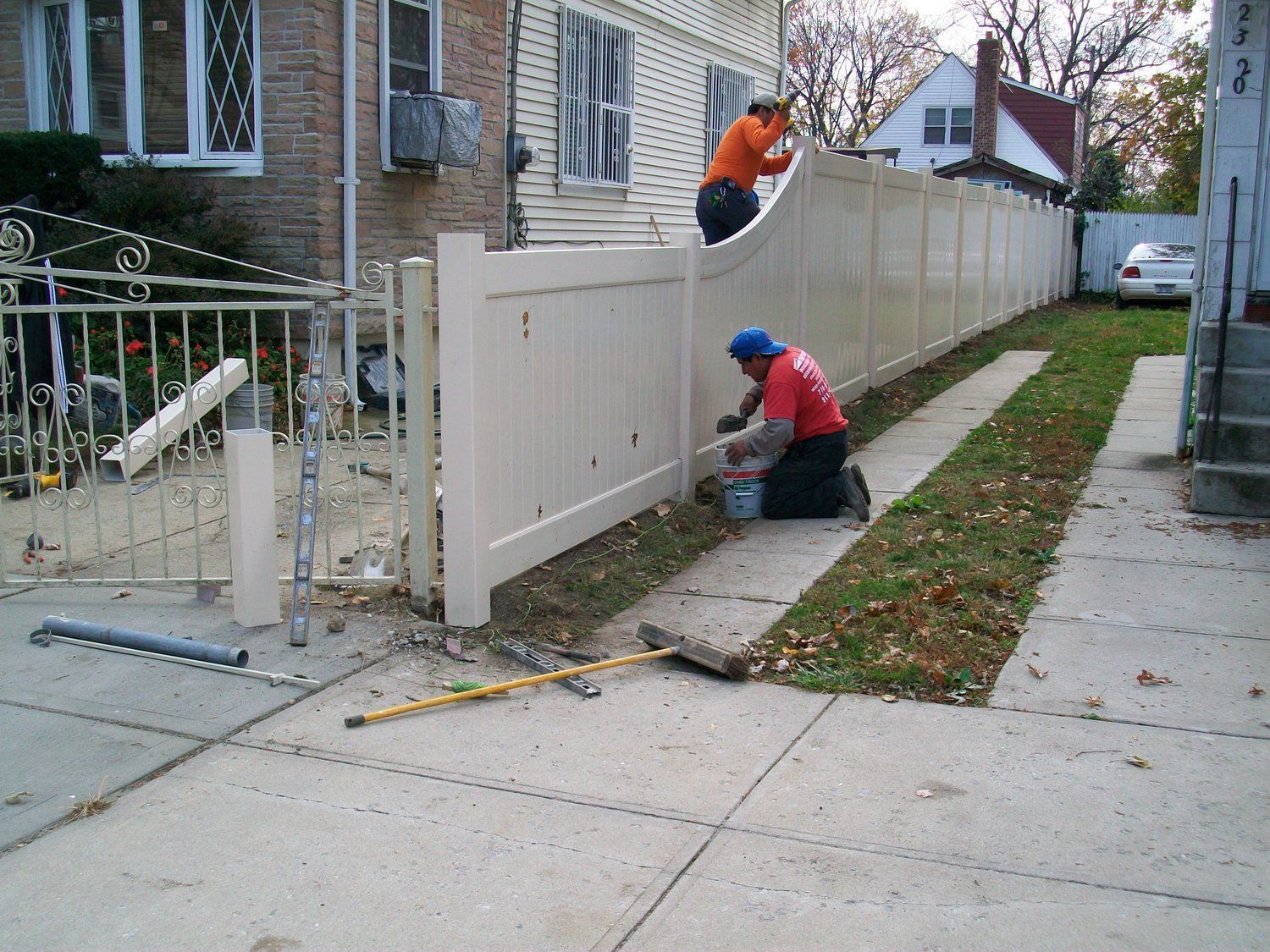 Two men are working on a white fence in front of a house