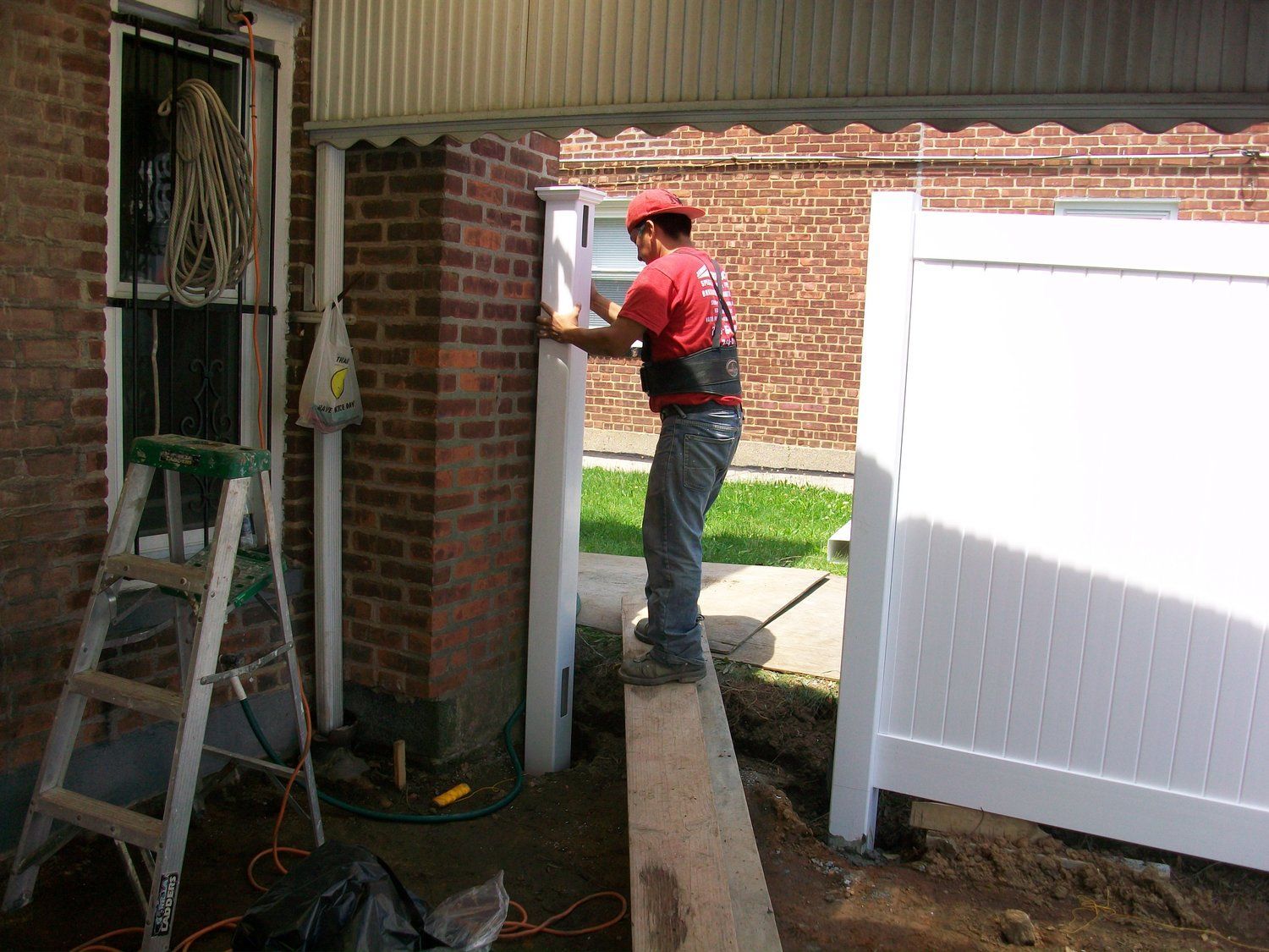 A man in a red shirt is working on a white fence