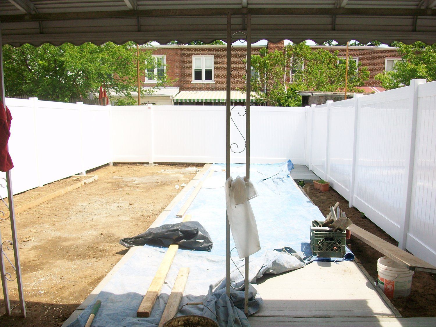 A white fence surrounds a dirt area with a brick building in the background