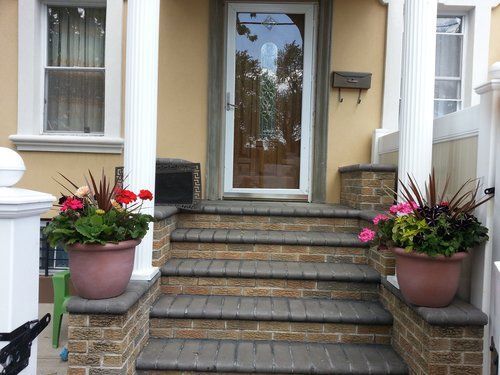 The front porch of a house with potted plants on the steps