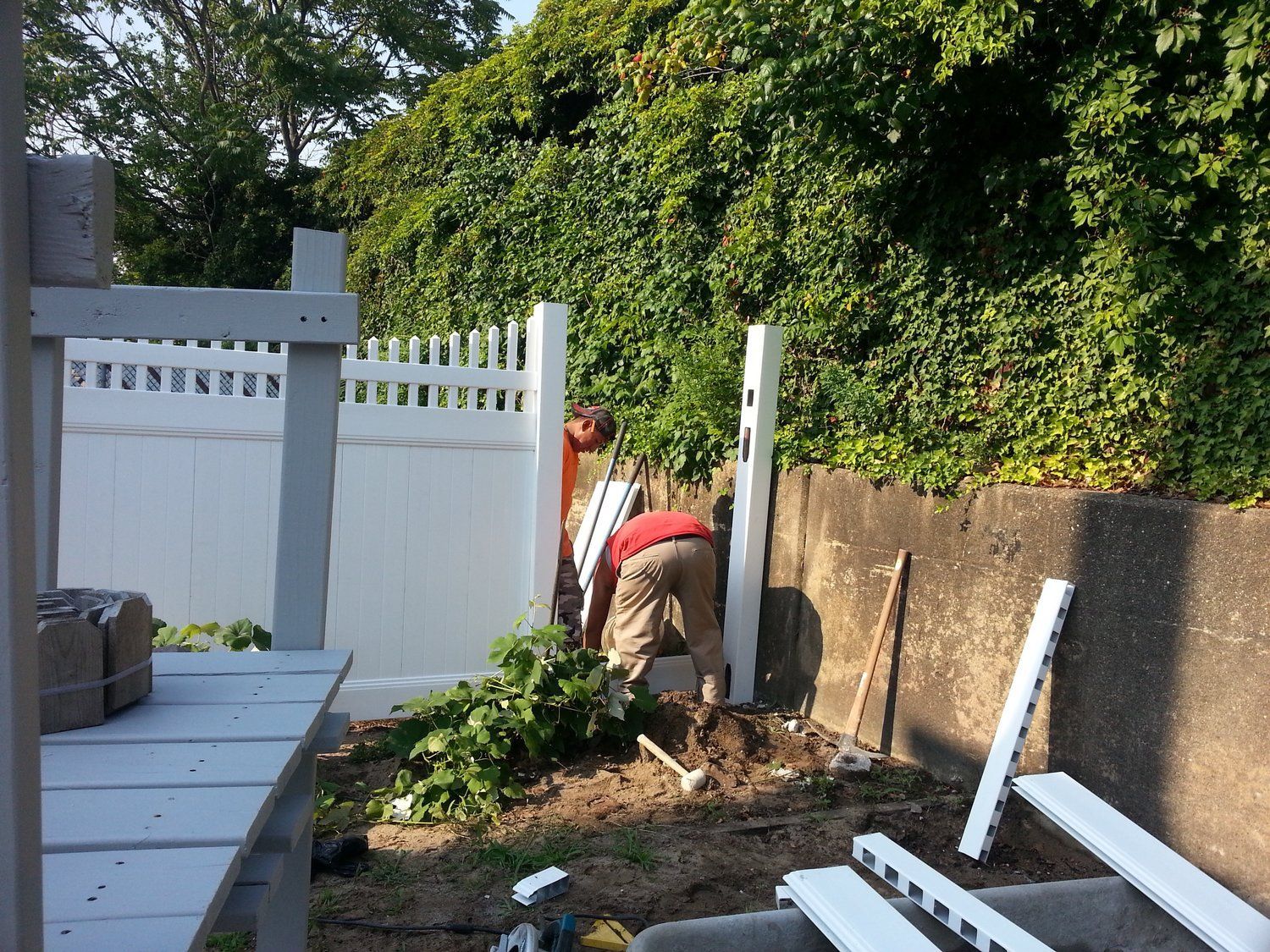 A man in a red shirt is working on a white fence