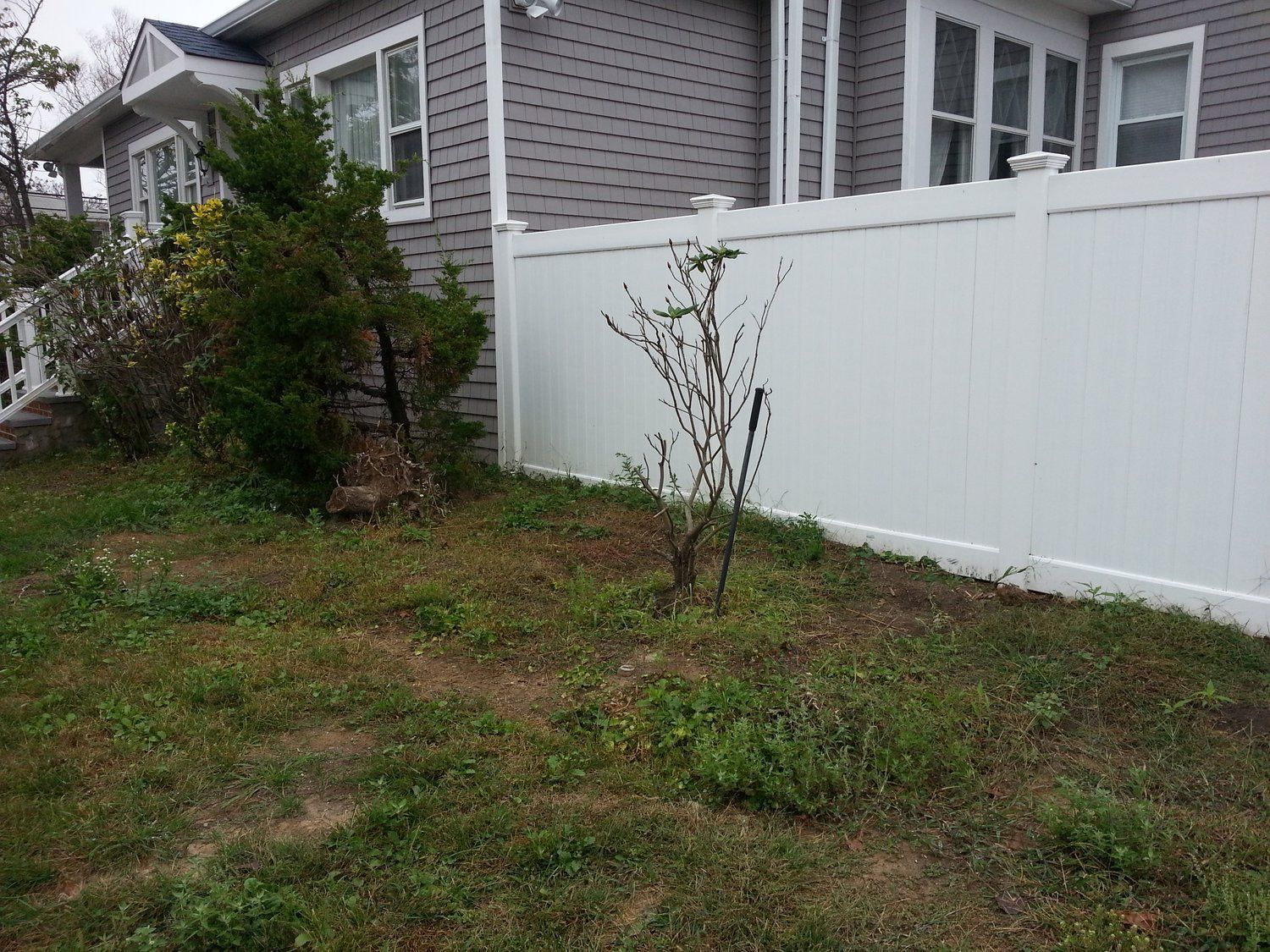 A white fence surrounds a lush green yard in front of a house.