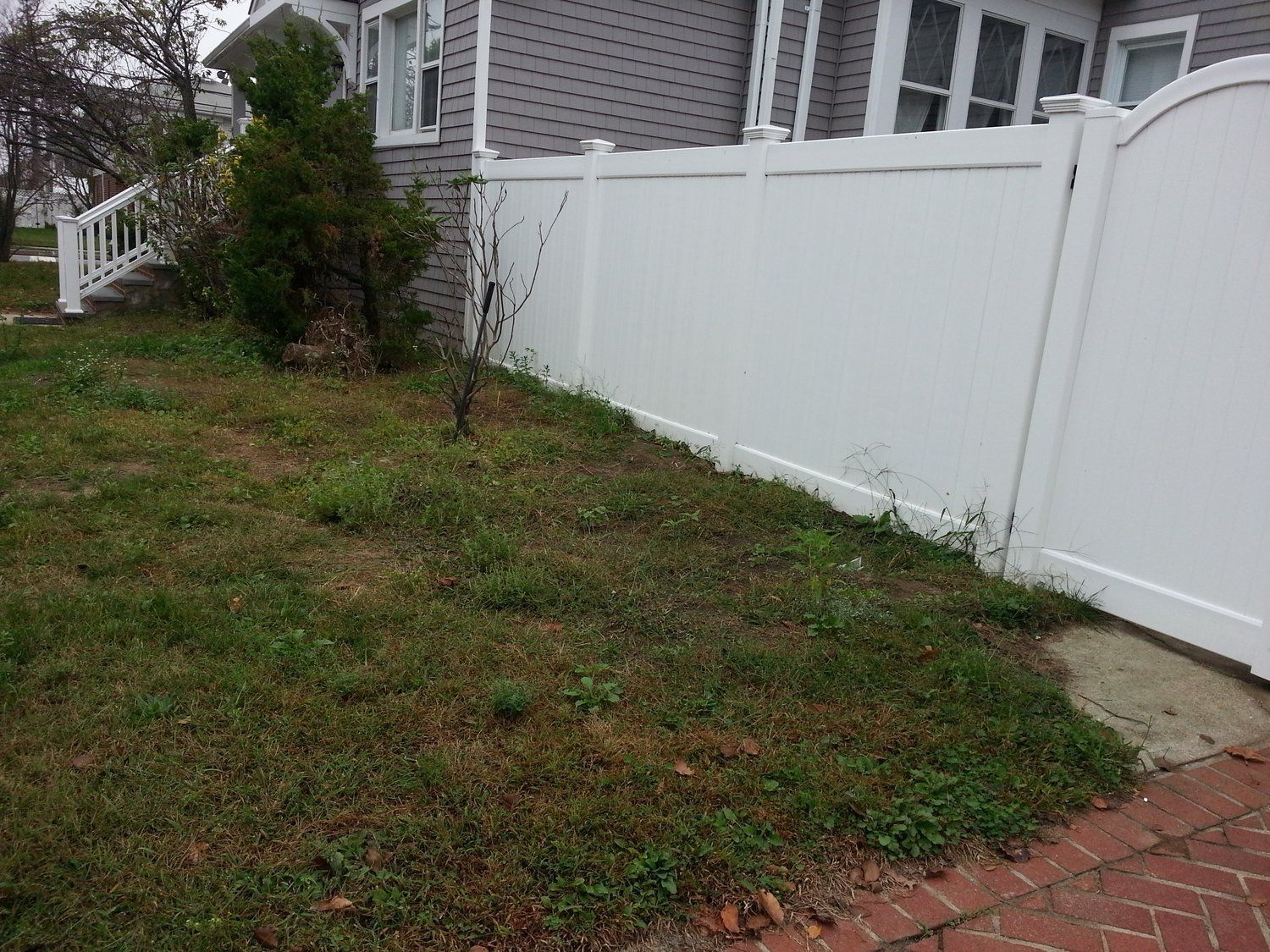 A white fence surrounds a lush green yard in front of a house.