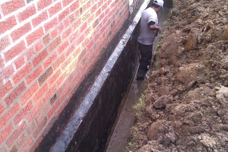 A man is standing in the dirt next to a brick wall.