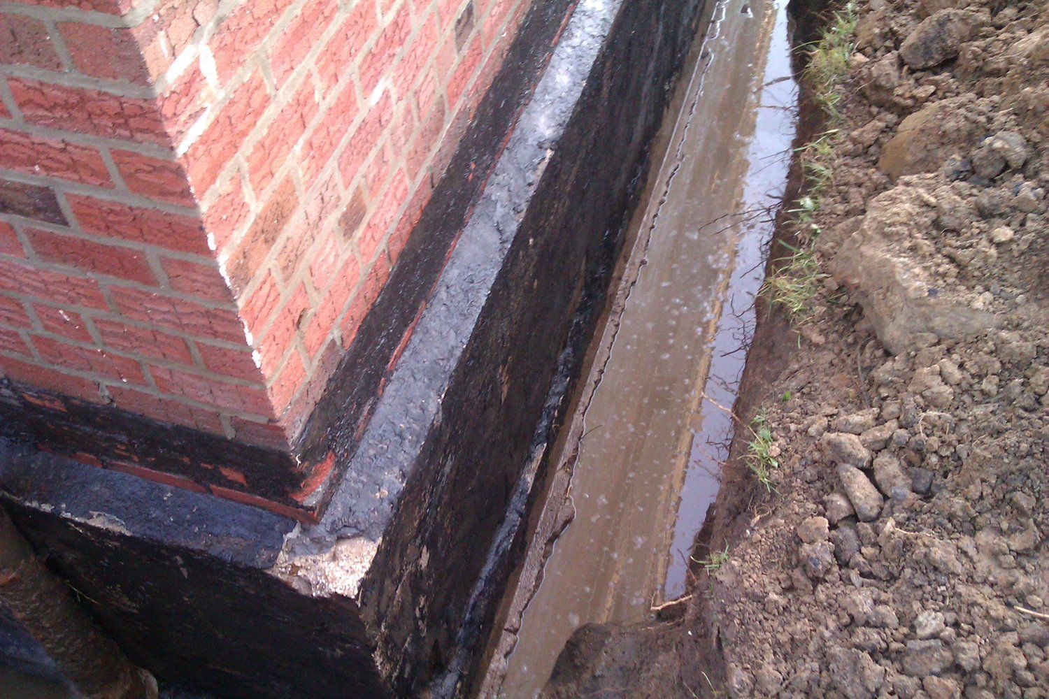 A brick wall with a black border is surrounded by dirt and water.