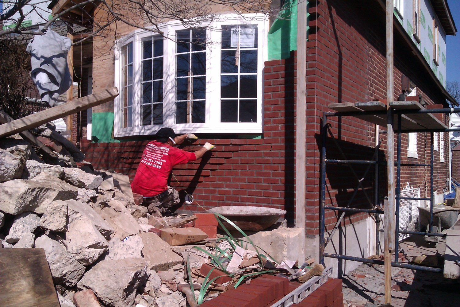 A man in a red shirt is working on a brick wall
