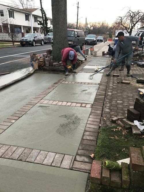 A man is laying concrete on a sidewalk next to a tree.