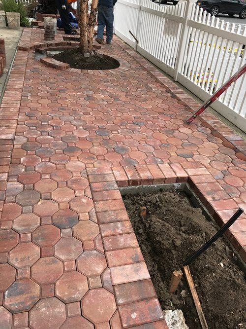 A brick walkway is being built next to a white fence.