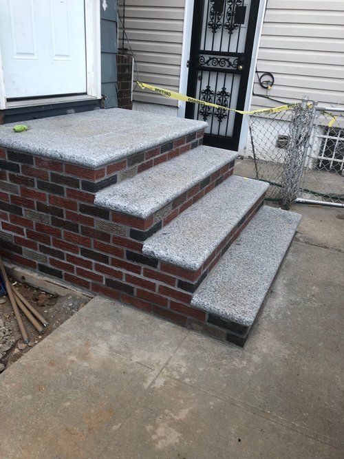 A brick porch with granite steps is being built in front of a house.