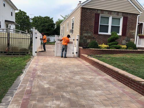 Two men are working on a driveway in front of a house.