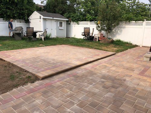 A man is standing next to a brick patio in a backyard.