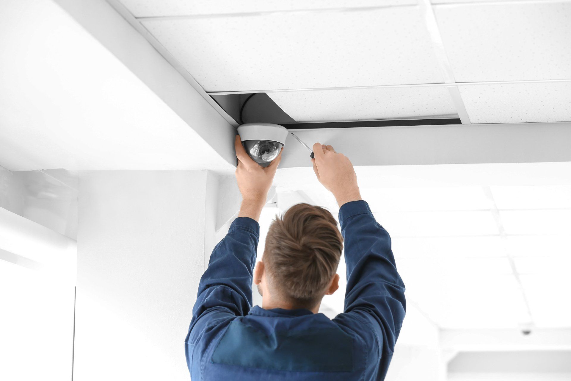 A man is installing a security camera on the ceiling.