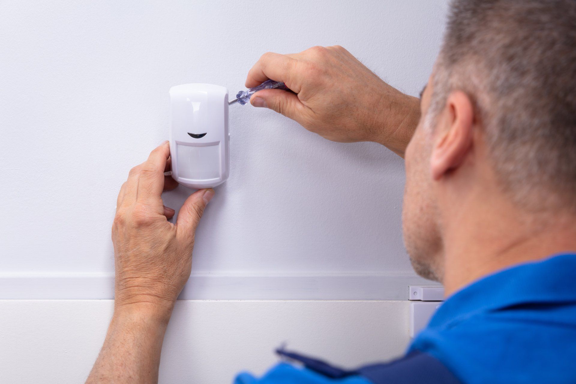 A man is installing a security system on a wall.