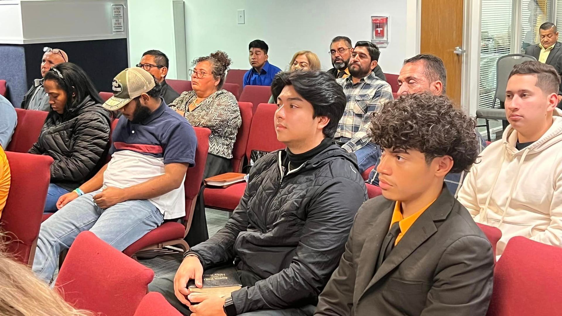 Un grupo de personas están sentadas en sillas rojas en una habitación.