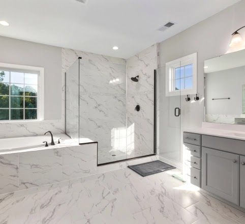 Bathroom with white marble tile, glass shower, grey vanity, and window.