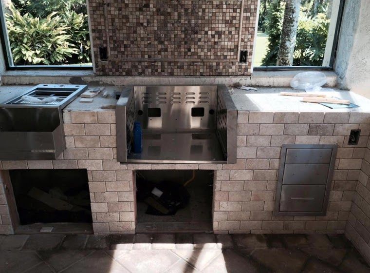 Outdoor kitchen with brickwork, stainless steel appliances, and tile backsplash.