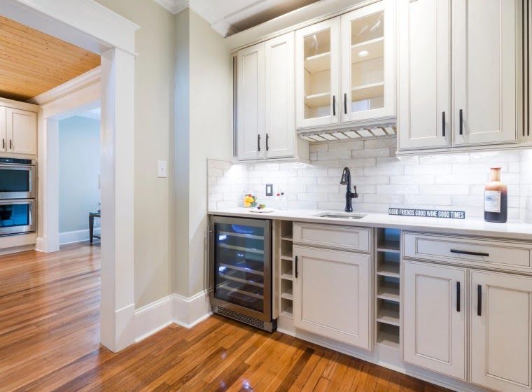 A small, built-in bar area with white cabinets, a wine fridge, and a sink.