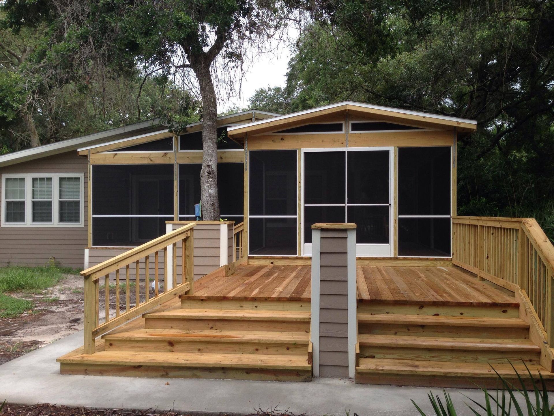 Screened porch with wooden deck and stairs, attached to a tan house with a tree growing through it.